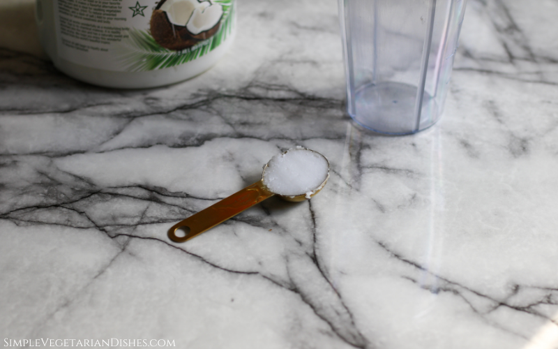 coconut oil in golden measuring spoon on white marble table