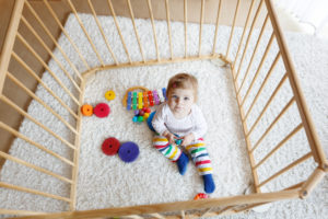 Beautiful little baby girl sitting inside playpen. Cute adorable child playing with colorful toy